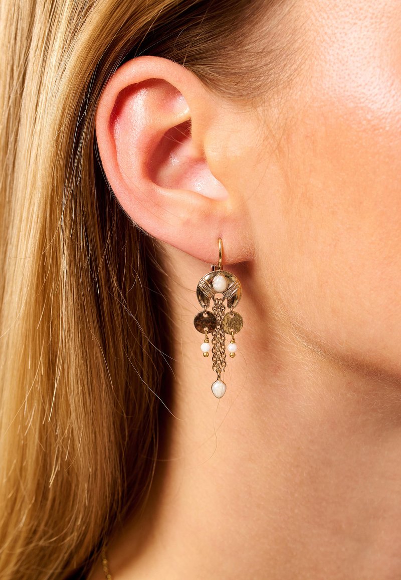 Boucles d'oreilles dorées avec des accents circulaires, des chaînes et des perles au fini texturé, suspendues en dessous du lobe de l'oreille.