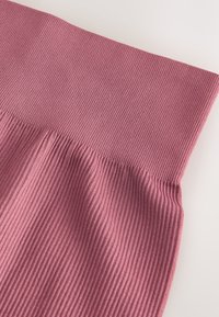 Drapiatura z prążkowanej dzianiny w jasnoróżowym kolorze, charakteryzująca się gładką fakturą i elastycznym pasem. Projekt podkreśla delikatne fałdy i kontury.