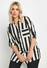 Camicia a righe bianco e nere con taschino sul petto, maniche arrotolate e vestibilità comoda. Realizzata in tessuto leggero.