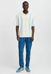 Polo corto de color amarillo claro con rayas verticales azules y cuello, acompañado de unos jeans azules y zapatillas azules con acentos blancos.
