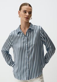Overhemd met een lichtblauw en marineblauw verticaal streep patroon. Gemaakt van gladde stof, met een kraag en lange mouwen.