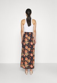 Jupe longue fleurie avec un fond bleu marine, ornée de motifs floraux orange et jaune, une ceinture et un tissu fluide.