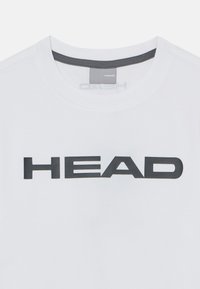 Bela majica s kratkimi rokavi, okrogli izrez, z velikim črnim logotipom "HEAD" čez prsni del. Gladka tekstura tkanine.