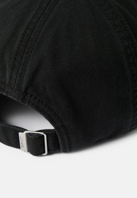 Cappellino da baseball in tessuto nero con visiera curva, materiale testurizzato e una fibbia in metallo argentato sul retro, che presenta il nome del marchio "GANT."