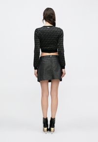 Pulover negru scurt cu design de logo cu model, asortat cu o mini-fustă din denim închis la culoare și cizme negre cu toc și gleznă.