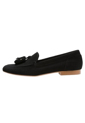 Mocassin en suède noir avec détail pompon sur le dessus et talon plat marron clair, vue latérale sur fond blanc.