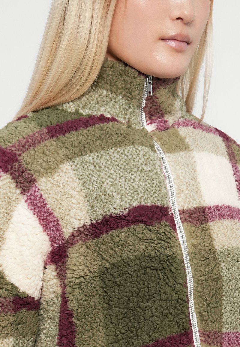 Giacca in pile con colletto alto e chiusura con zip, caratterizzata da un motivo a patchwork nei colori verde, crema e bordeaux.