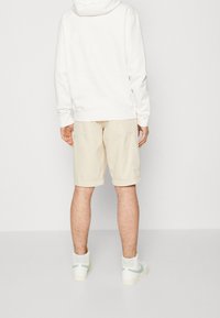 Pantalones cortos cargo beige con dos bolsillos laterales, combinados con una sudadera con capucha blanca. Zapatillas blancas con acentos verdes. Textura no visible.