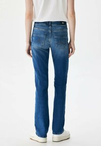 Modri jeans iz denim materiala s ravno zasnovo, ki vključujejo dve zadnji žep in subtilne šive. Nošeni z belimi supergami.