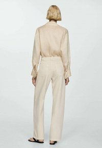 Cămașă din in bej cu mâneci lungi și manșete deschise, asortată cu pantaloni largi cu talie înaltă, bej deschis. Design simplu și curat, fără anumite embellismente.