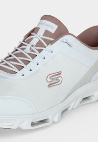 Baskets Skechers blanches et beiges en tissu mesh, design à lacets, semelle coussinée avec aérations et logo sur la tige latérale.