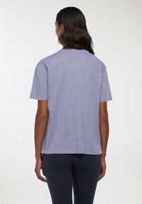 T-shirt corto a maniche corte di colore viola chiaro in tessuto morbido, con una vestibilità comoda, scollo rotondo e orlo dritto, senza motivi o accessori visibili.