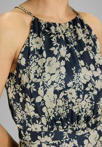 Laivansininen kukallinen mekko, jossa on kermavärinen kukkakuosi. Mekossa on poimutettu rintaosa ja ketjut olkaimissa. Sileä kangastuntu.