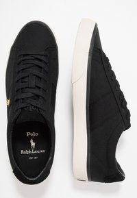 Svarta tygskor med texturerad ovandel, kontrasterande beige gummisula och svarta snören. Har gulddetaljer med logotyp på sidan.