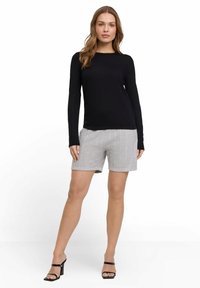 Haut à manches longues noir assorti à un short texturé gris clair avec des rayures verticales. Le mannequin porte des talons aiguilles noirs.