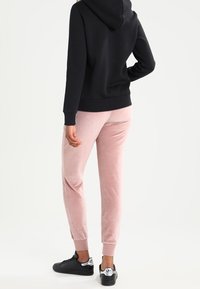 Svart hoodie med en känguruficka, kombinerad med rosa velourbyxor och svarta sneakers. Hoodien har snörning och ribbade muddar.