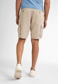 Beige cargoshorts met zijzakken, gestructureerde linnen stof en een relaxte pasvorm. Gecombineerd met witte sneakers en een lichtblauw shirt.