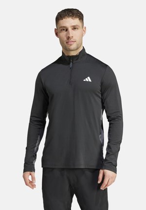 Camiseta atlética negra de manga larga con cremallera, hecha de un tejido ligero y suave con un sutil brillo y un logo blanco en el pecho.