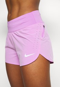 Ljusrosa träningsshorts med hög midja, böjd nederkant, sidoficka med dragkedja och små ventilationshål, med en vit Nike-logotyp.