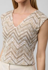Texturiertes beiges und weißes Oberteil mit V-Ausschnitt, kurzen Ärmeln und einem Zickzackmuster aus leichtem, luftigem Stoff.