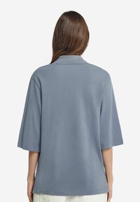 Kortärmad skjorta med krage i mjukt blått tyg. Avslappnad passform med en slät textur och nederkant som faller något under midjan.
