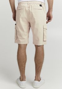 Shorts cargo roses avec une taille élastique, deux poches cargo latérales et des poches arrière à patch, associés à des baskets blanches.