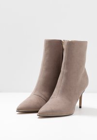 Szare zamszowe botki sięgające kostki z ostrym noskiem, zapinane na zamek z boku i z cienkim wysokim obcasem. Gładka tekstura z minimalną ilością detali w designie.