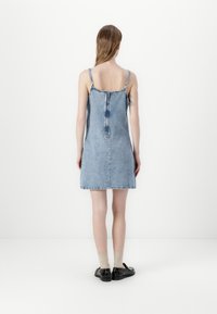 Traper haljina u svijetlop plavoj boji s podesivim naramenicama, prilagodljivim korzetom i razgibanim suknjom. Ima središnji zatvarač na leđima i sirovi rub.