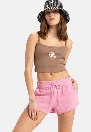 Brauner gerippter Crop-Top mit weißer Blumenstickerei, kombiniert mit pinken Shorts mit Kordelzug, fransigem Saum und seitlichen Taschen. Schwarzer und weißer Bucket Hat.