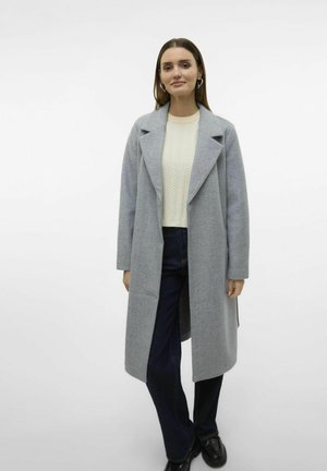 Abrigo de lana gris con cuello de muesca, abierto por delante y de mangas largas, usado sobre un suéter texturizado color crema y jeans oscuros de pierna ancha.