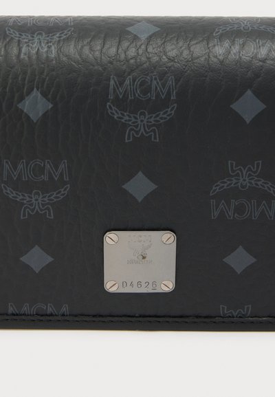 Μαύρο δερμάτινο πορτοφόλι με ανάγλυφο μοτίβο λογότυπου MCM, ασημένια μεταλλική πλακέτα με την επιγραφή «München» και σειριακό αριθμό, λεία υφή.