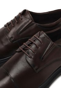 Bruine leren nette schoenen met een gladde textuur, klassieke vetersluiting en subtiele stikdetails op de bovenkant en zijkanten.