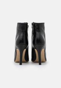 Botines de cuero negro con un diseño elegante, tacones altos de aguja, cremalleras laterales y una textura suave. Estilo minimalista con punteras puntiagudas.