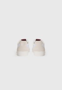 Zapatillas de gamuza beige y piel blanca con acentos en burdeos en el talón. Punta redondeada y suela de goma plana, diseño minimalista.