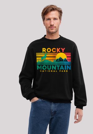 Mann trägt einen schwarzen Sweatshirt mit einem bunten Design "Rocky Mountain National Park", das einen Hirsch, Berge und einen untergehenden Sonnen zeigt.
