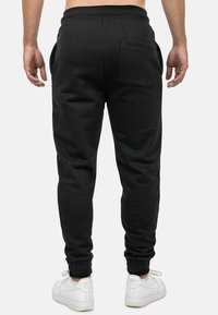 Zwarte joggingbroek van zacht materiaal, met een tapered fit, elastische tailleband, zijzakken en een enkele achterzak.