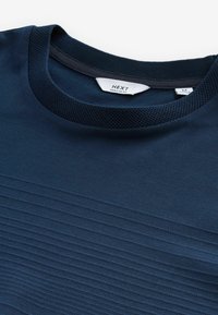 Mørkeblå t-shirt med korte ærmer og en tekstureret mesh-krave, som har vandrette ribbede linjer over hele kroppen, lavet af blødt stof.