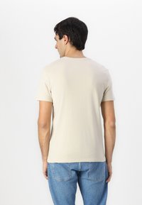 Beige T-Shirt mit kurzen Ärmeln und Rundhalsausschnitt, aus Baumwolle gefertigt. Trägt man zu blauen Jeans, was ein schlichtes, lässiges Design zeigt.