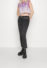 Virkat väst i ljuslila med droppmönster, ihopparat med svarta raka jeans med färgglad metalldetaljer och svarta, kraftiga ankelskor.