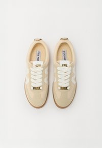 Sneakers di un beige chiaro con superiore in maglia, dettagli bianchi, hardware dorato sulla linguetta e suola in gomma testurizzata. Design classico con lacci.