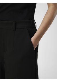 Pantalon noir taille haute avec un design structuré, doté de poches latérales, d'une texture lisse et de détails élastiques à la ceinture.