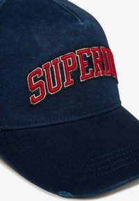 Gorra azul marino hecha de una mezcla de algodón con un logo bordado de "SUPERDRY" en rojo y dorado. Visera curvada con detalle de costura.