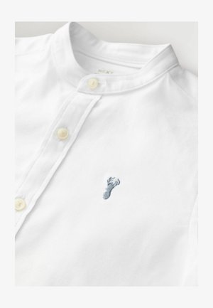 Valge särk püstkraega, millel on kaks kreemikat nööpi ja vasaku rinna piirkonnas väike sinine tikand hirve kujutisega.