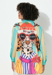 Chemise à col avec un graphique de chien coloré. Présente des rayures bleues, jaunes et beiges, et un motif festif et ludique. Le matériau semble lisse et léger.