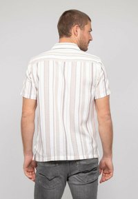 Chemise à manches courtes rayée en blanc et beige avec une finition texturée. Elle dispose d'un col pointu et d'un ourlet droit avec des fentes latérales.