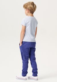Helles blaues T-Shirt mit kurzen Ärmeln, kombiniert mit lila Sweatpants, die über gerippte Bündchen und Seitentaschen verfügen. Weiße Freizeit Sneakers runden das Outfit ab.