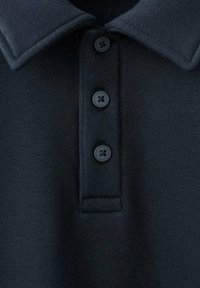 Granatowa koszulka polo o miękkiej fakturze, z klasycznym płaskim kołnierzykiem oraz trzema czarnymi guzikami do zapinania.