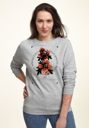 Grauer Sweatshirt mit floraler Grafik in Rot und Grün. Mit gerippten Bündchen und Hals. Das Model posiert mit der Hand auf der Hüfte und zeigt das Design.