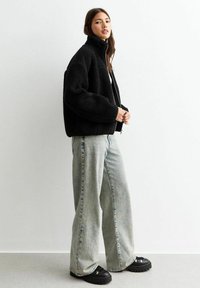 Svart fleecejacka med hög krage, oversized passform. Kombinerad med ljusblå, vida denimjeans och svarta plattformssneakers.