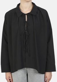 Zwarte blouse met een kraag en voorste strikjes, voorzien van lange mouwen en een losse pasvorm. Zachte stof met een gladde textuur.